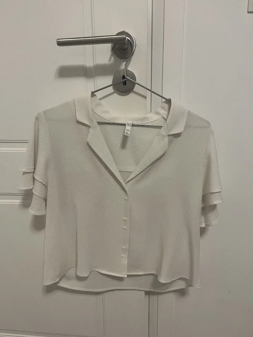 Blusa blanca de manga corta con volados en las mangas y botones al frente. Talle S, ideal para un look fresco y elegante.