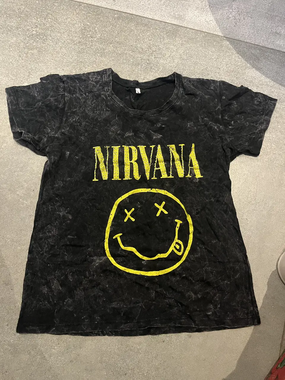 Remera de hombre con estampado de Nirvana y el icónico smiley. De color negro con efecto lavado, ideal para un look rocker y casual. Talle L.