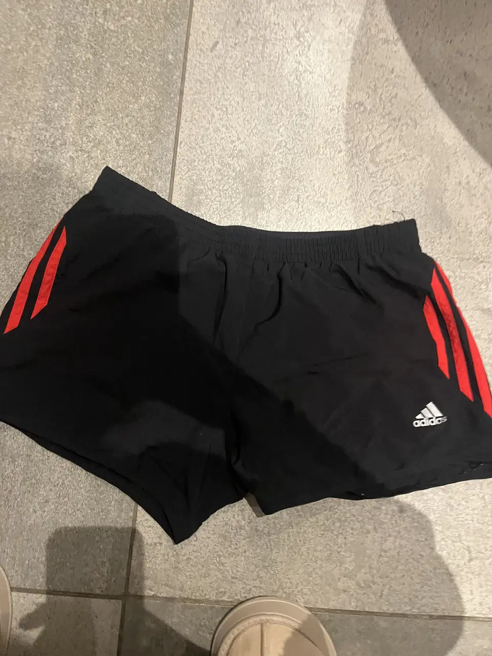 Short deportivo Adidas negro con detalles en rojo. Ideal para running y entrenamientos.