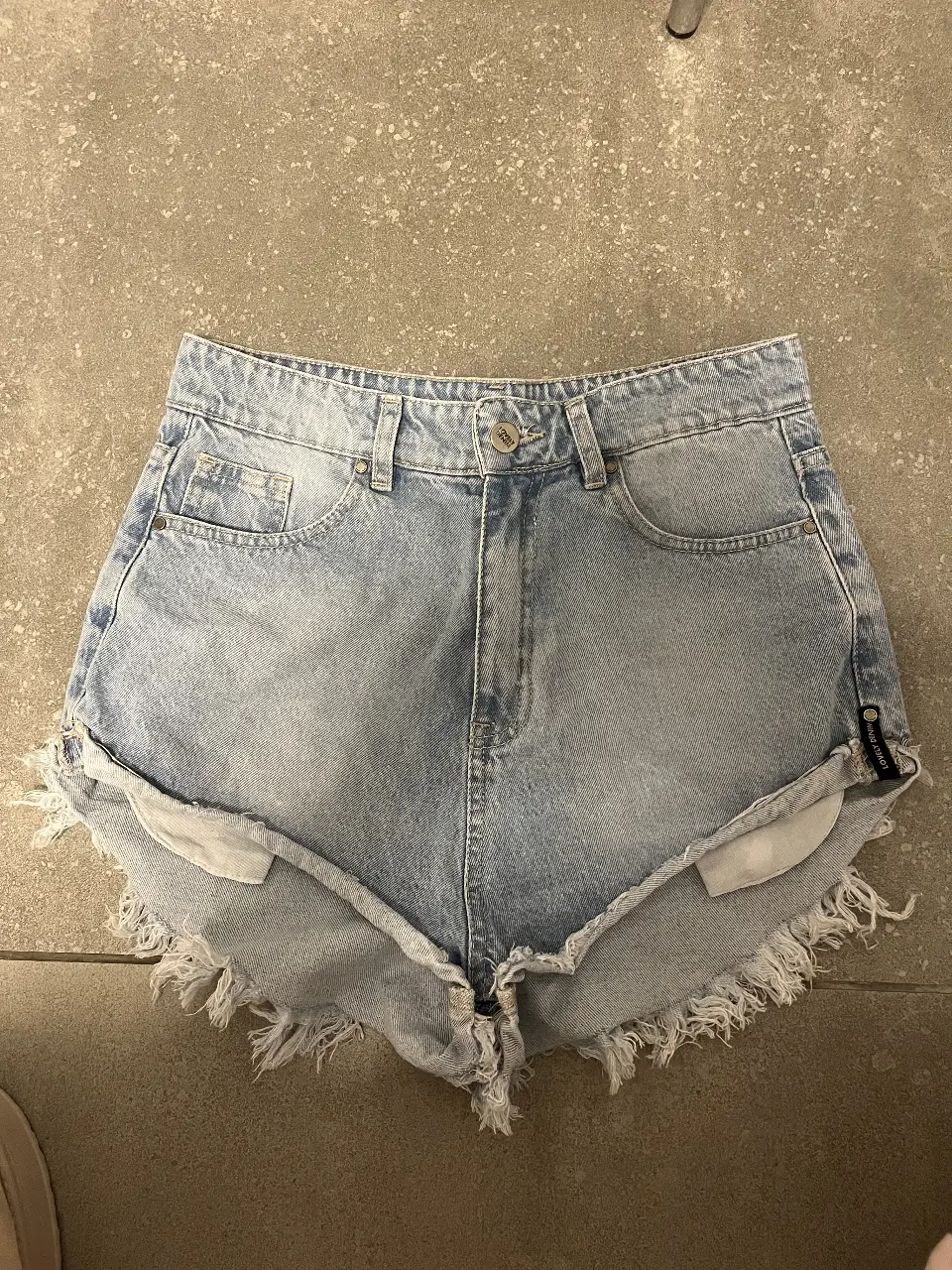 Short de jean de mujer, tiro alto, con flecos en el borde. Talle 26. Marca Lovely Denim.