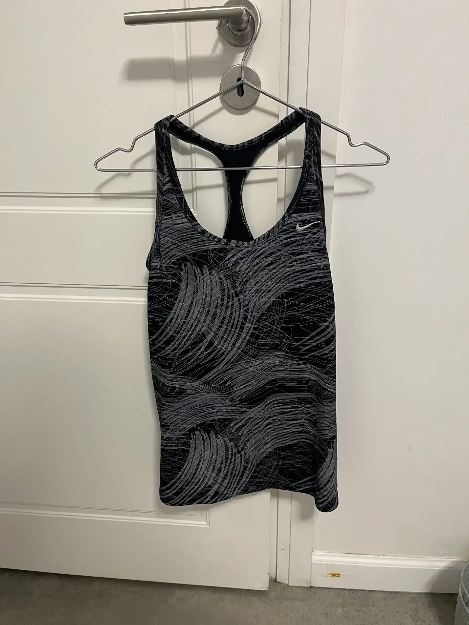 Musculosa deportiva Nike Dri-Fit para mujer, con estampado abstracto en tonos grises y negros. Ideal para entrenamientos y actividades físicas.