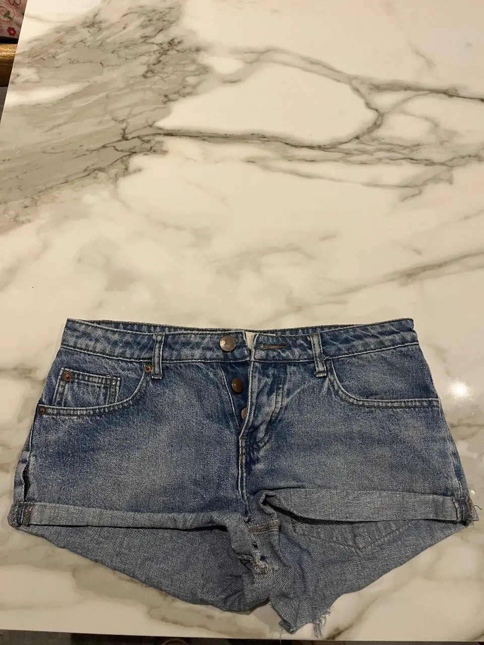 Short de jean azul claro, tiro medio, con detalles de desgaste y dobladillo en los bordes. Ideal para un look casual y fresco.