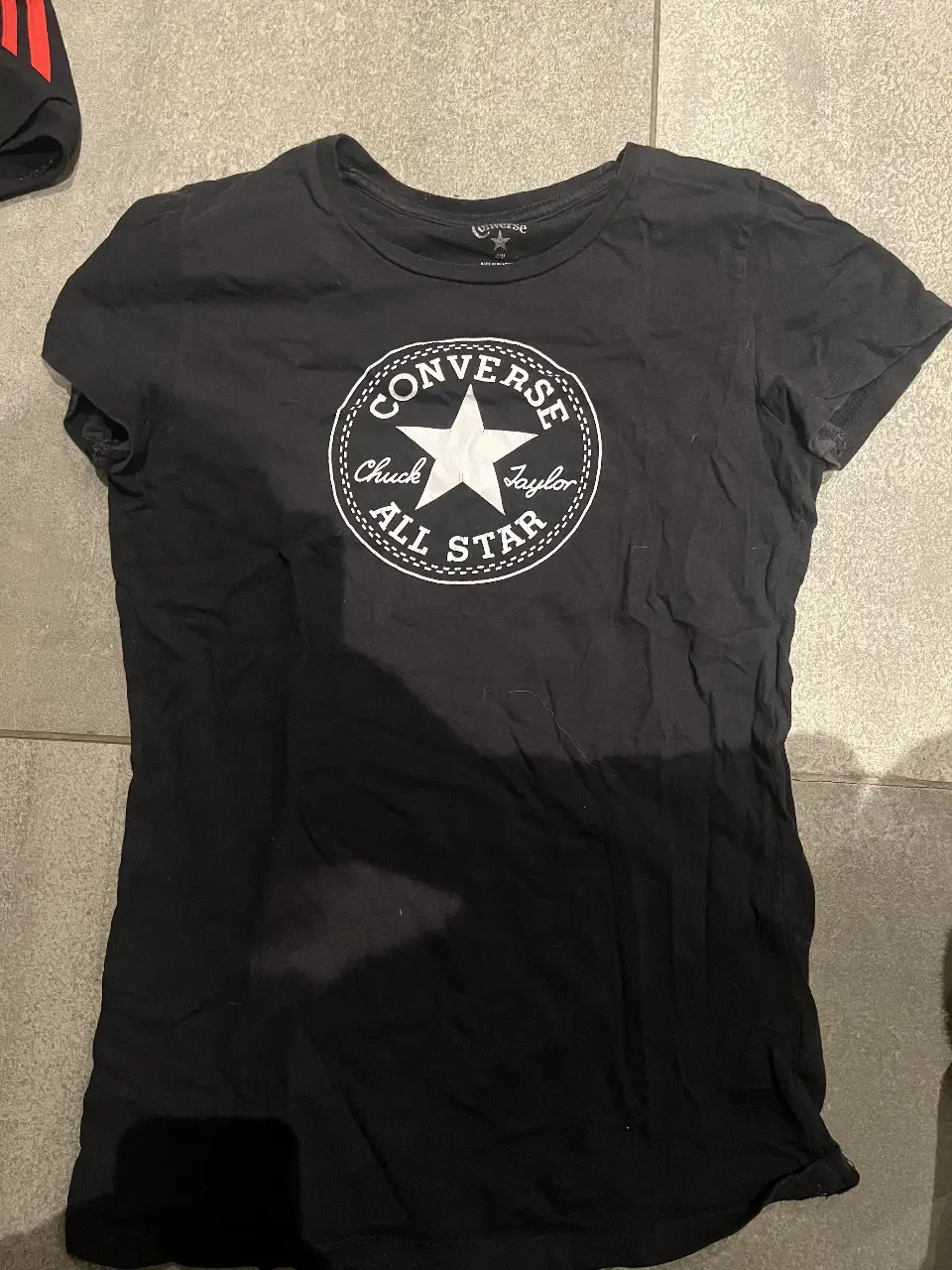 Remera negra de mujer con estampado del logo de Converse Chuck Taylor All Star en blanco. Ideal para un look casual y cómodo.