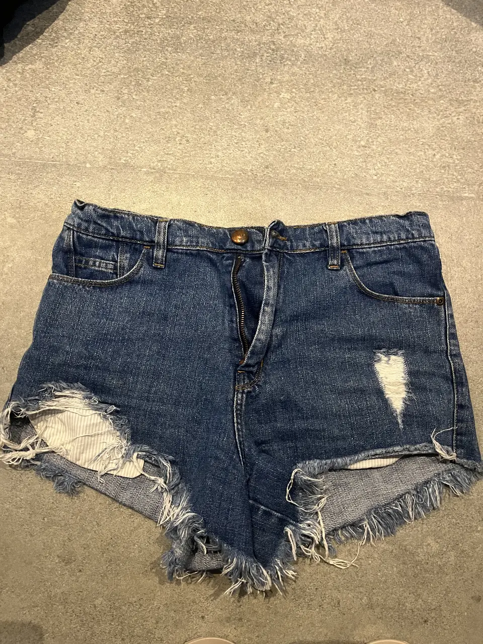 Short de jean azul con roturas y flecos en el borde. Tiro medio, ideal para un look casual y moderno. Marca Cher.