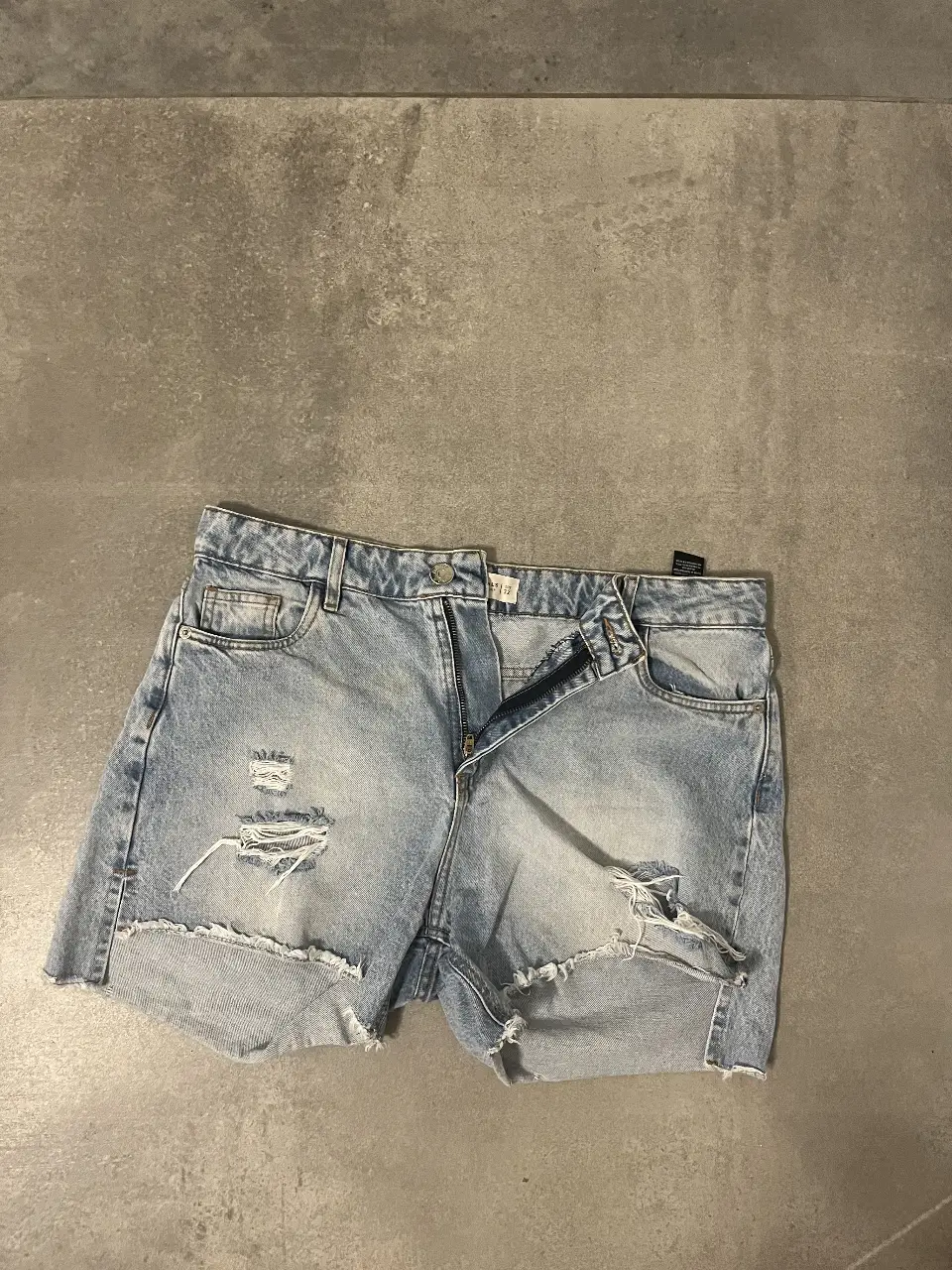 Short de jean de mujer, tiro medio, con roturas y detalles desflecados. Talle 32. Marca Batuk Originals.