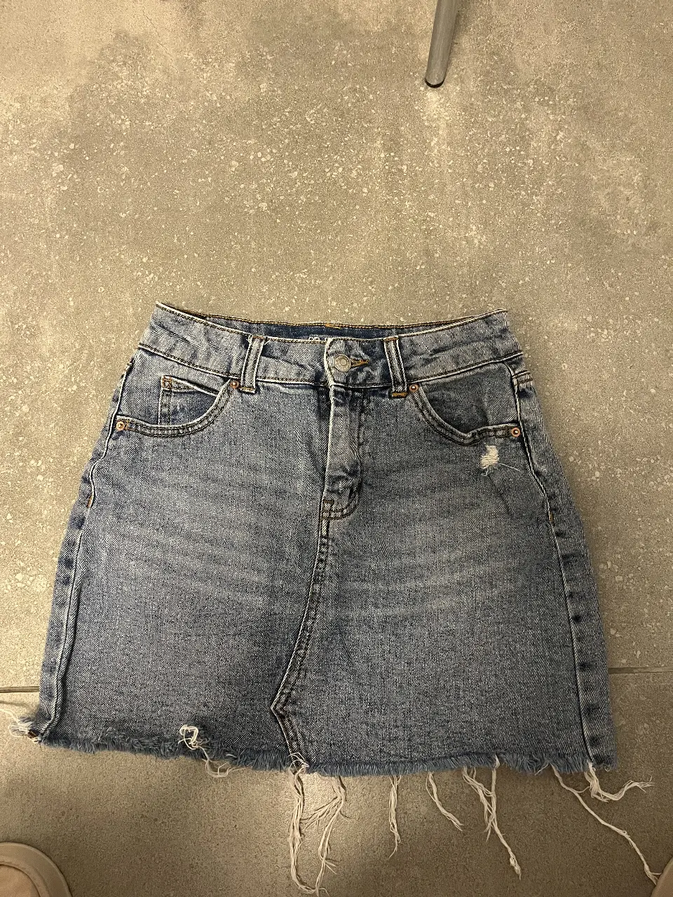 Pollera de jean larga, con detalles de roturas y flecos en el borde inferior. Ideal para un look casual y moderno.