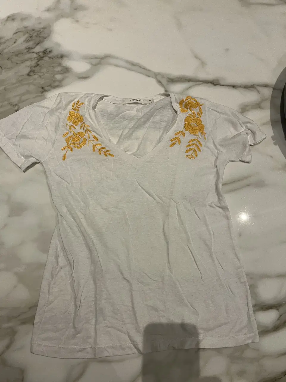 Remera blanca de mujer con cuello en V y bordado floral amarillo en la parte delantera. Ideal para un look casual y fresco.