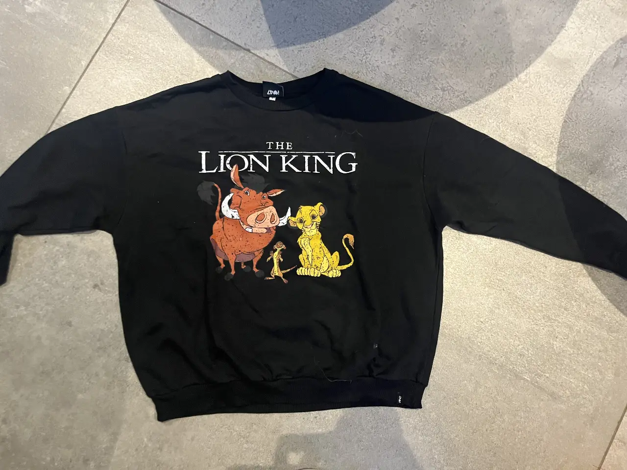 Buzo de cuello redondo negro de "The Lion King" con estampado de Timón, Pumba y Simba. Producto oficial de Disney Classics.