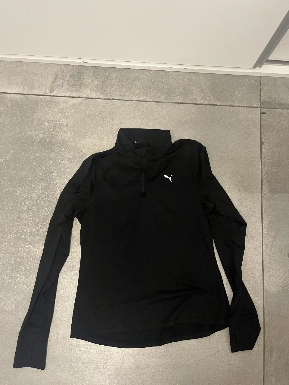 Remera deportiva de manga larga para hombre, color negro, con cierre en el cuello y logo de Puma en el pecho. Ideal para running y entrenamiento.
