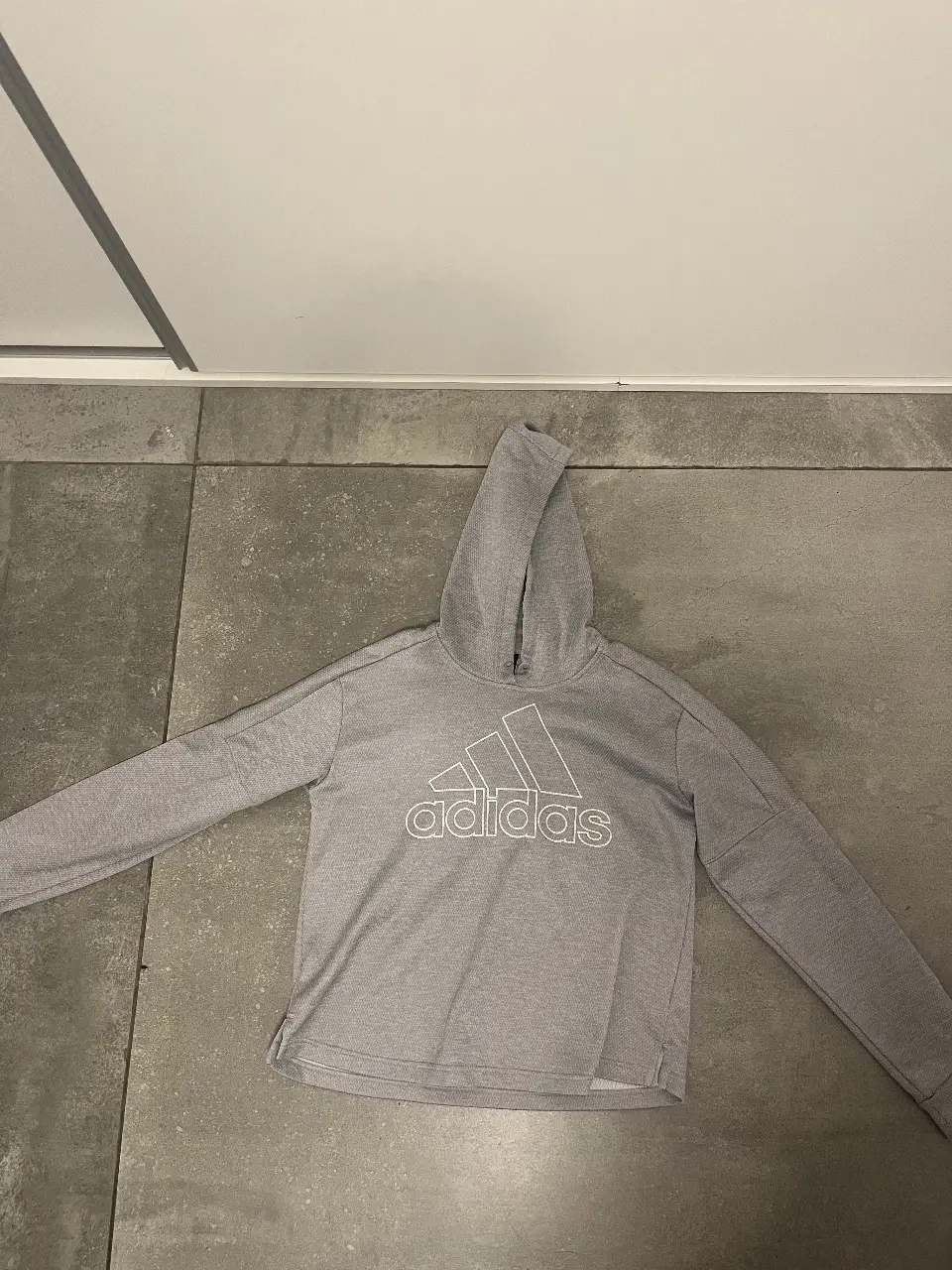 Buzo deportivo Adidas gris con capucha y logo blanco. Ideal para actividades físicas o uso casual.
