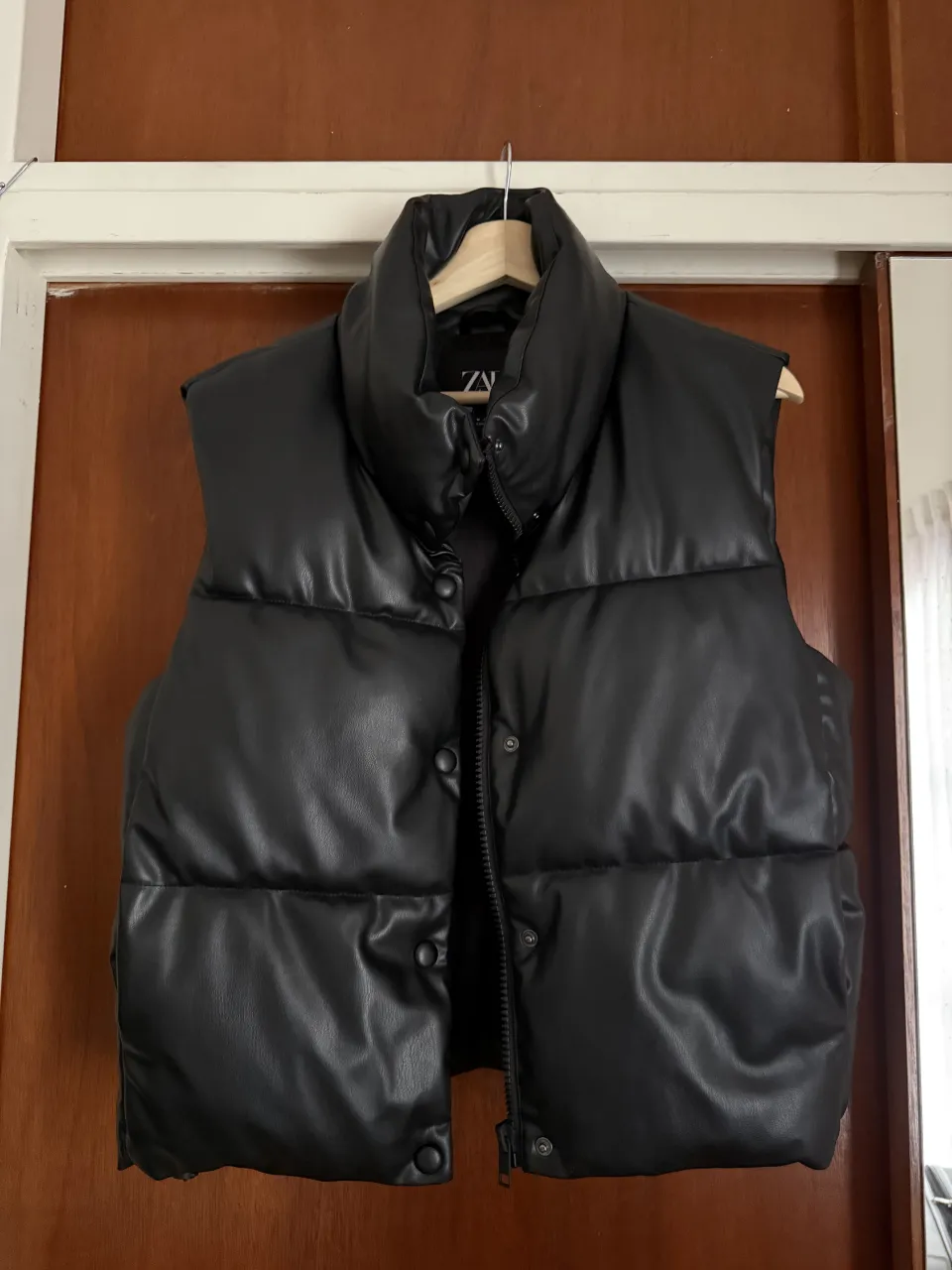 Chaleco acolchado negro de cuero sintético con cuello alto y botones a presión.