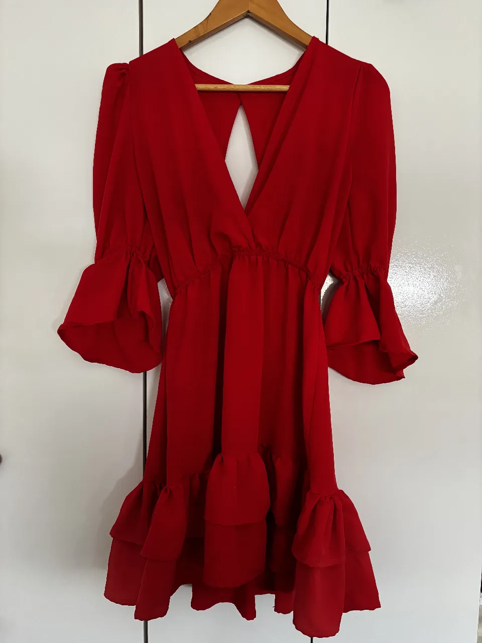 Vestido mini rojo con escote en V y espalda descubierta. Mangas largas con volados en los puños y falda con volados. Ideal para una fiesta o evento especial.