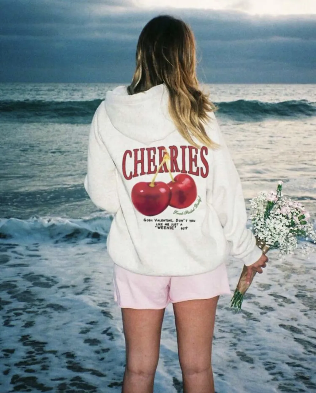 Buzo canguro blanco con estampado de cerezas en la espalda. Diseño con capucha y detalles en rojo. Ideal para un look casual y cómodo.