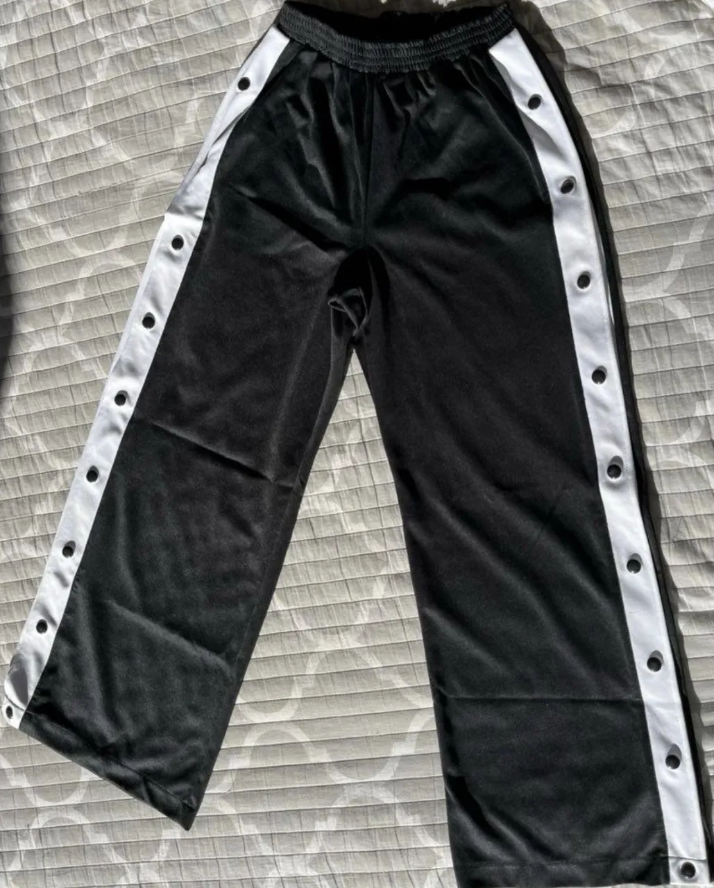 Pantalón deportivo negro con detalles blancos en los laterales y botones. Ideal para un look casual y cómodo.
