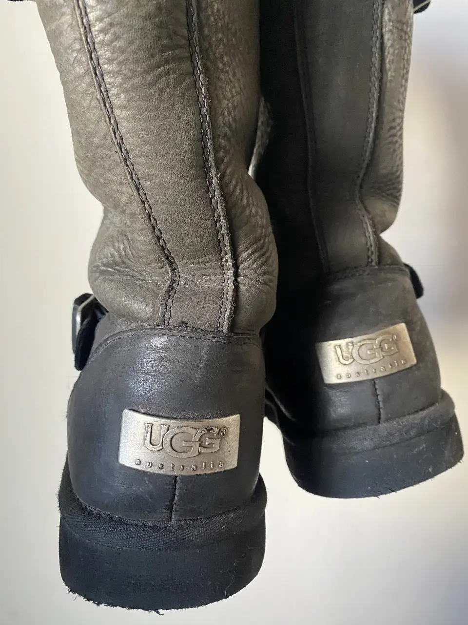 Botas UGG de cuero negro con detalles de hebillas y logo plateado. Interior de piel de oveja, ideales para el invierno.