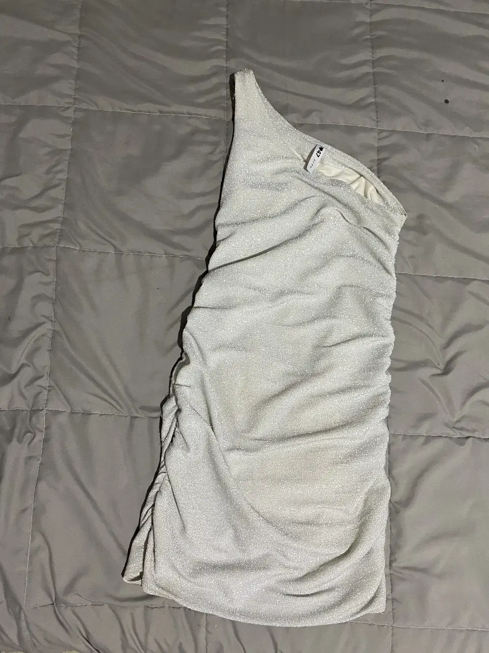 Vestido mini plateado de un solo hombro, ideal para fiestas y eventos especiales. Confeccionado con un tejido brillante y drapeado que realza la figura.