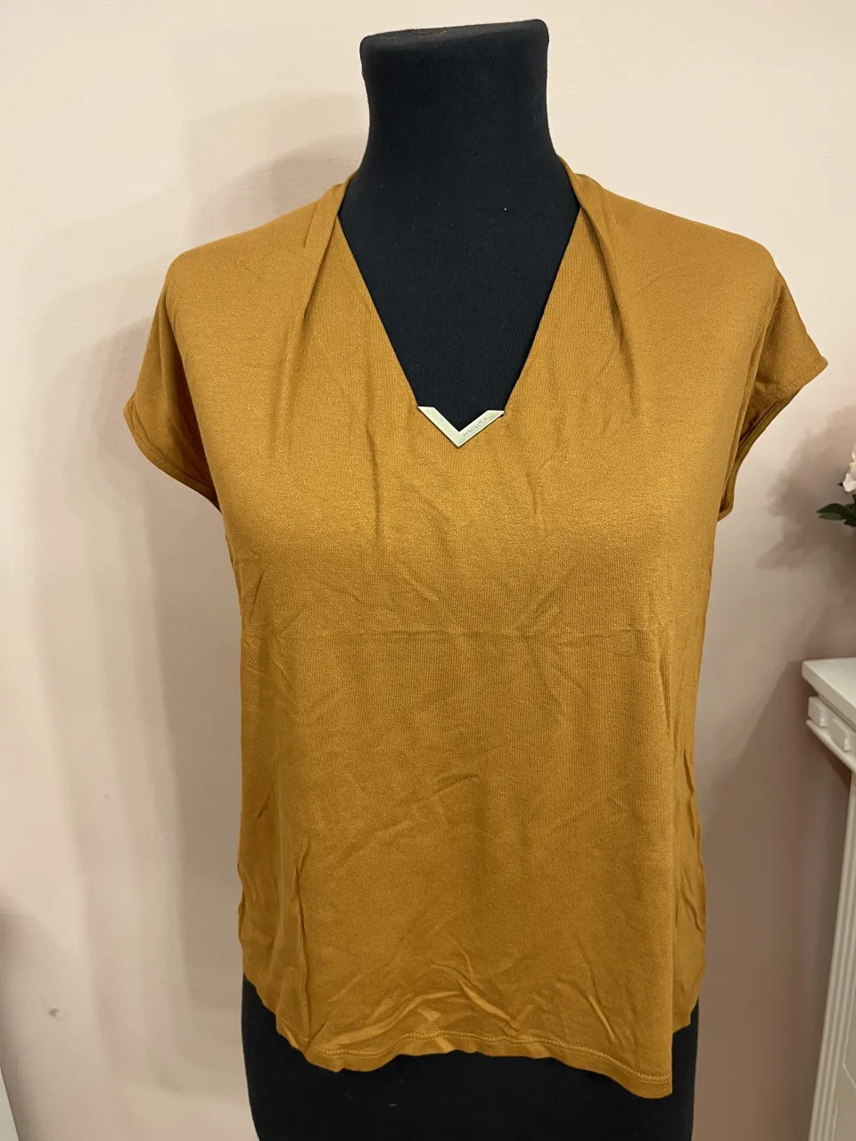 Remera de manga corta con cuello en V y detalle metálico en el escote. Diseño liso. Nueva sin uso 