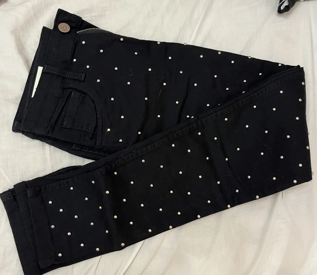 Jeans negros con tachas plateadas distribuidas por toda la prenda. Cierre y botón metálico.