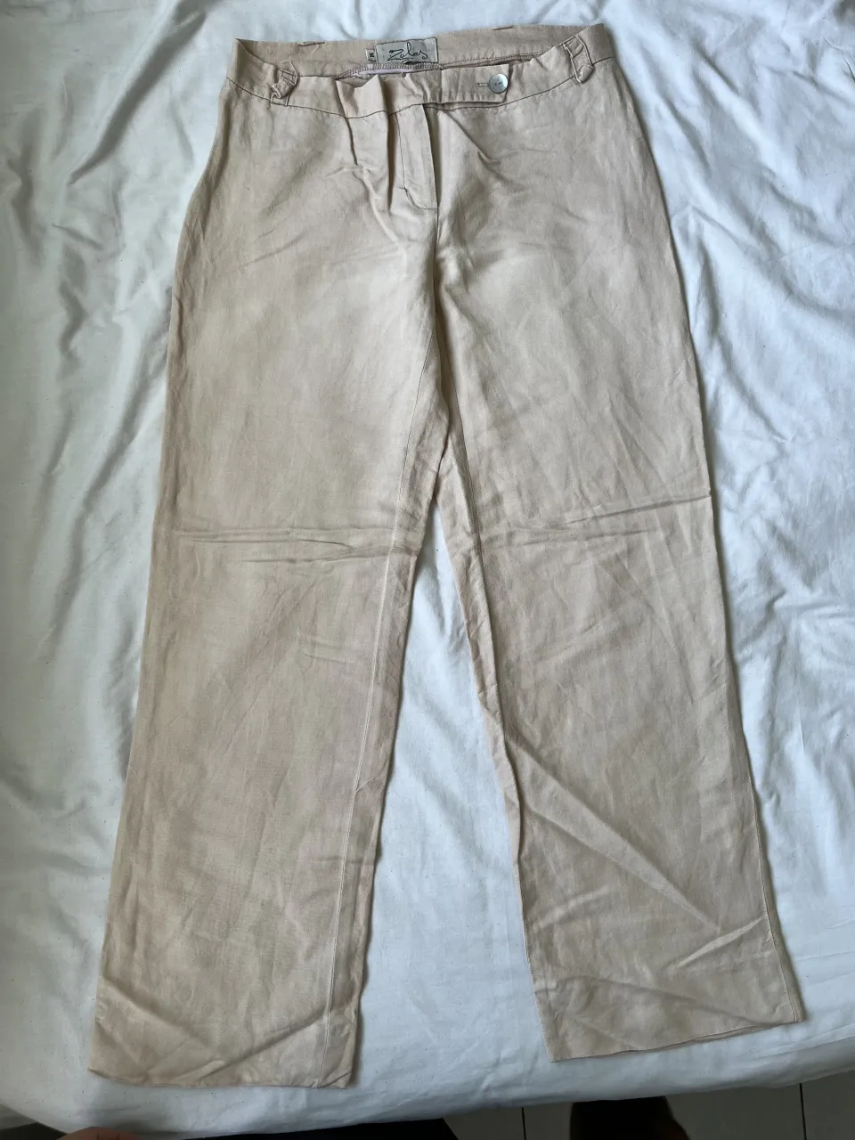 Pantalón de vestir color crudo, tiro alto, con detalles de botones en la cintura y bolsillos traseros. Diseño clásico y versátil, ideal para un look elegante o casual.