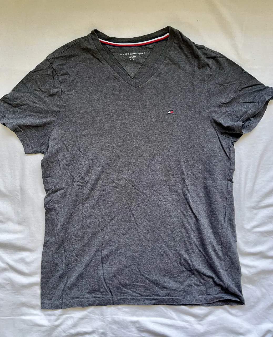 Remera gris de manga corta con cuello en V. Un clásico de la marca Tommy Hilfiger, ideal para el día a día. Perfecta para combinar con jeans o bermudas.