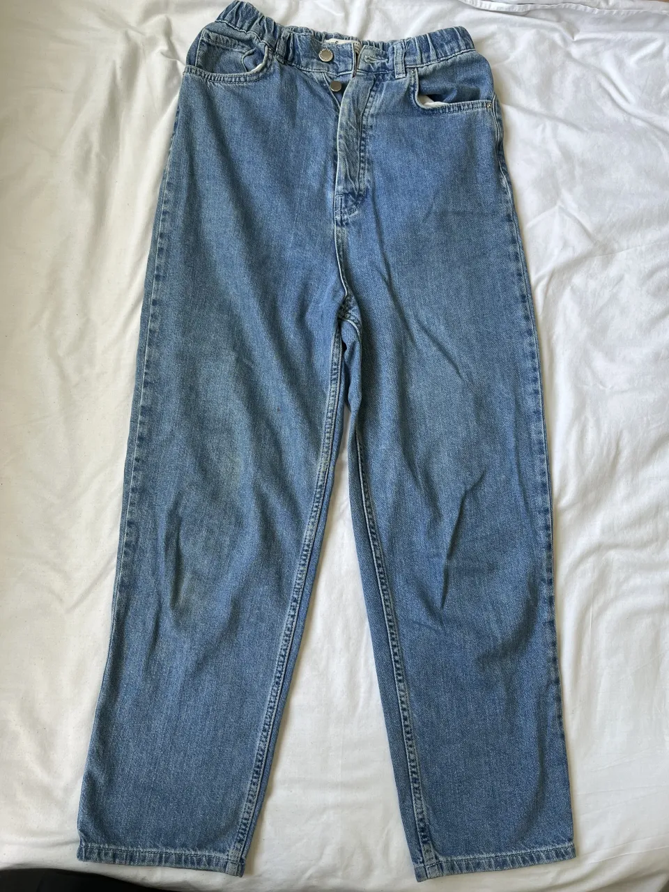 Jeans tiro alto con cintura elastizada y detalles de botones. Lavado clásico y corte recto, ideales para un look casual y cómodo.