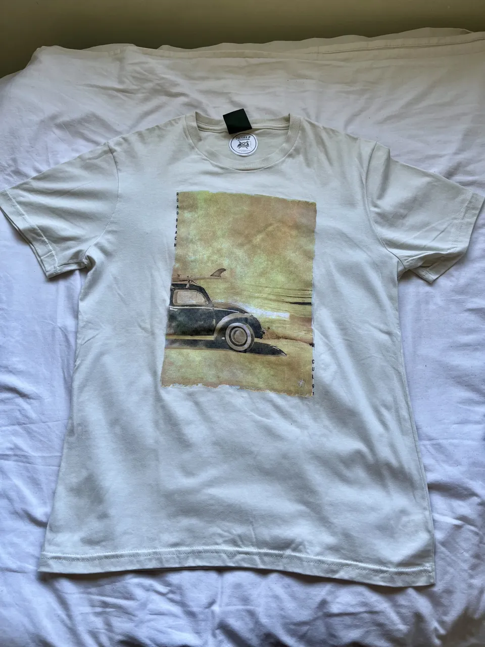 Remera de algodón color crudo con estampa vintage de un auto antiguo en la playa. Ideal para un look casual y relajado. Aunque es talle S tiene tamaño de M.