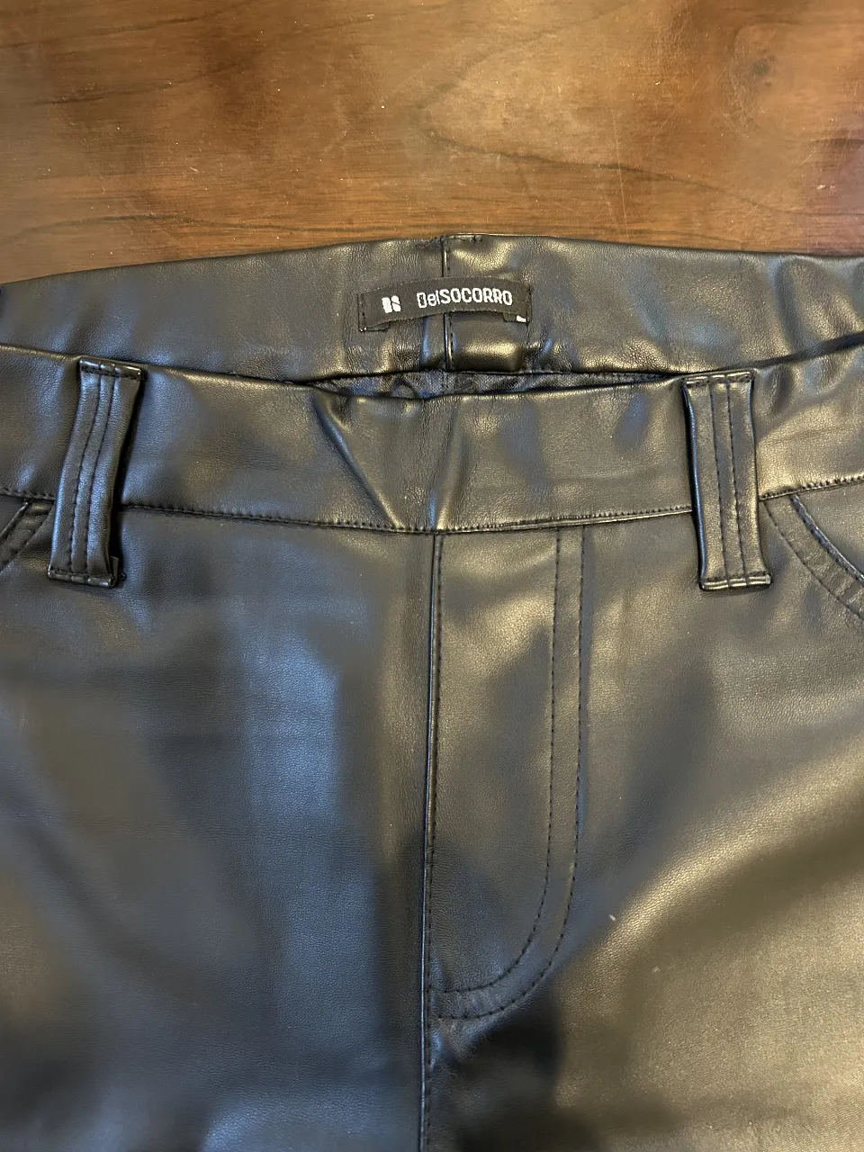 Pantalón de cuero sintético negro, tiro medio, con bolsillos delanteros y traseros. Ideal para un look moderno y sofisticado.