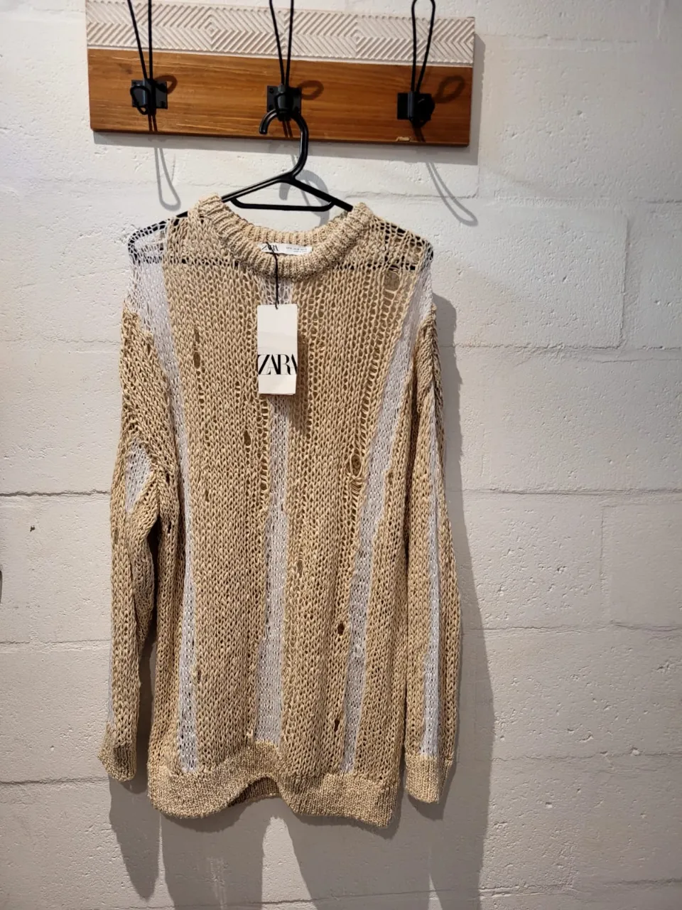 Sweater de tejido abierto con detalles de roturas y tiras verticales blancas intercaladas. Cuello redondo y mangas largas. oversize