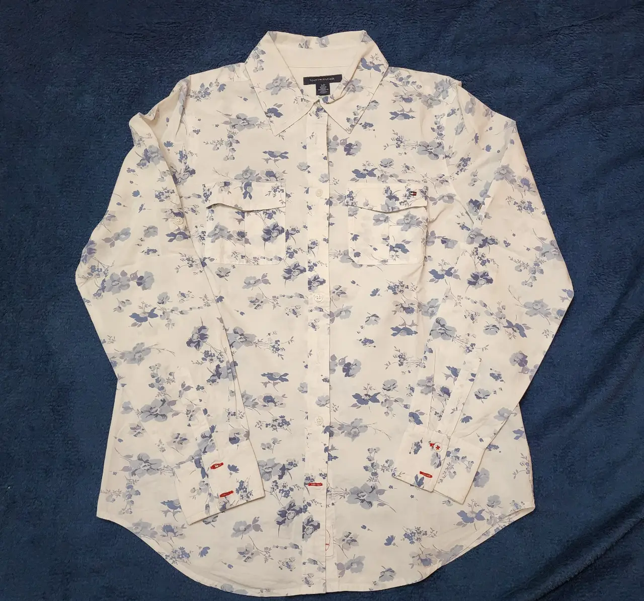 Camisa Tommy Hilfiger de mujer, blanca con estampado floral en tonos azules. Manga larga, con dos bolsillos delanteros y detalles en los puños. Ideal para un look casual y fresco.
