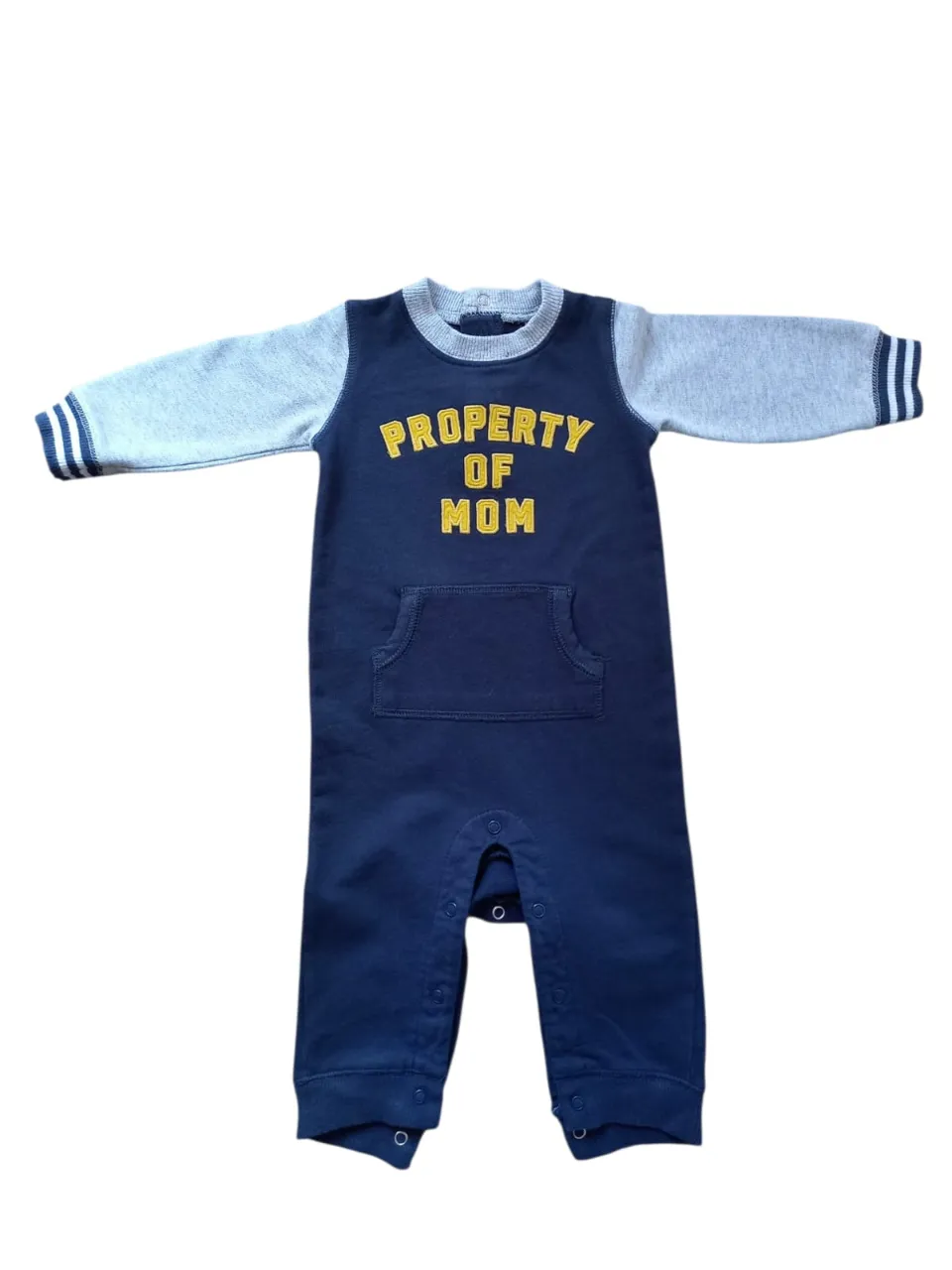 Enterito de bebé azul marino con mangas grises. Tiene la inscripción "PROPERTY OF MOM" en amarillo en el frente y un bolsillo tipo canguro. Las mangas tienen detalles a rayas en los puños.