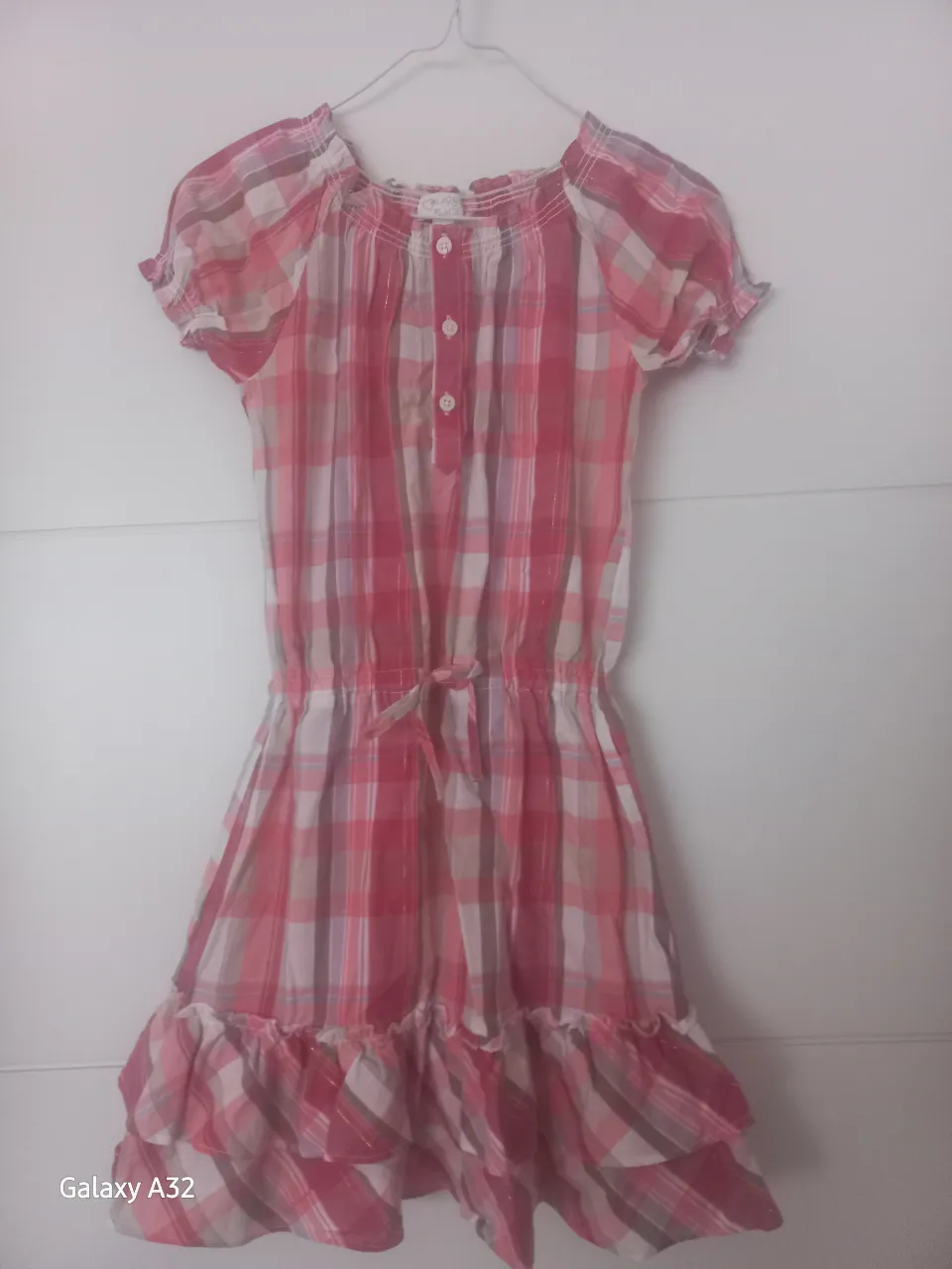 Vestido de niña a cuadros en tonos rosa y blanco, con detalle de volados en la falda y mangas cortas. Ideal para un look fresco y casual.