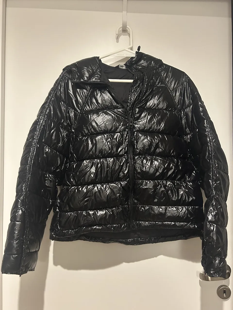 Campera de pluma negra brillante, con capucha y cierre. Ideal para el invierno, abrigada y con estilo.