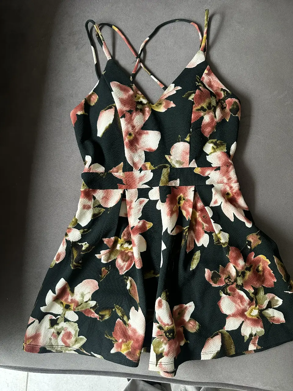 Vestido corto de mujer con estampado floral en tonos rosa y blanco sobre fondo negro. Diseño con tirantes cruzados en la espalda y detalle de fruncido en la cintura. Ideal para eventos y salidas.