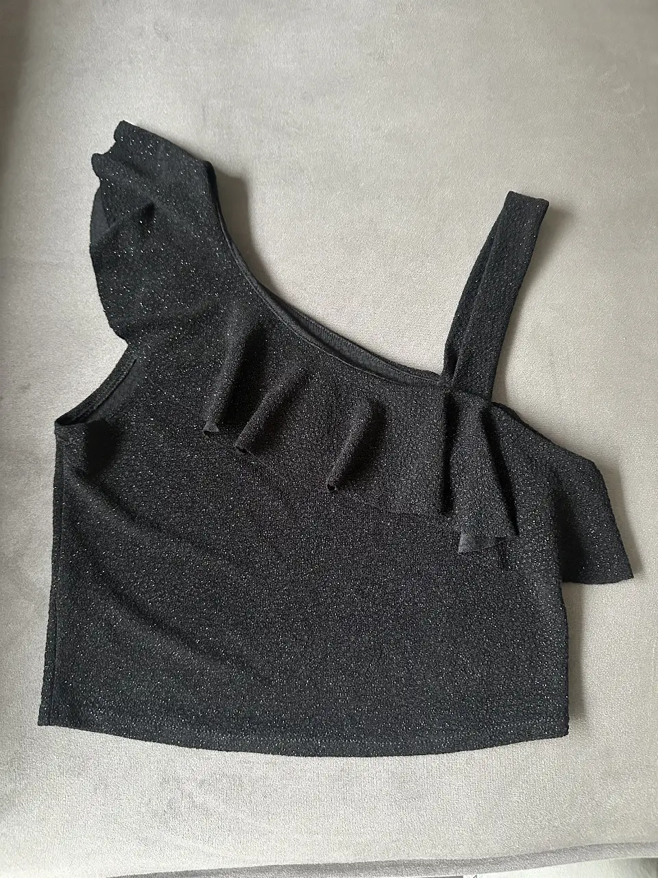 Top negro de brillito de un solo hombro con detalle de volado. Ideal para una salida o fiesta.