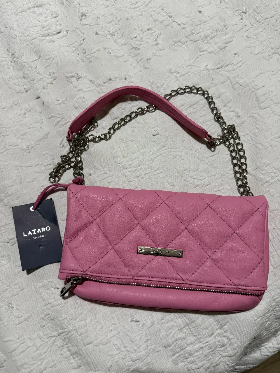 Cartera bandolera de cuero rosa con diseño acolchado marca Lázaro. Cuenta con cadena plateada y cierre. incluye bolsa de tela antipolvo para guardarla y espejo de la marca. Ideal para un look casual y moderno.