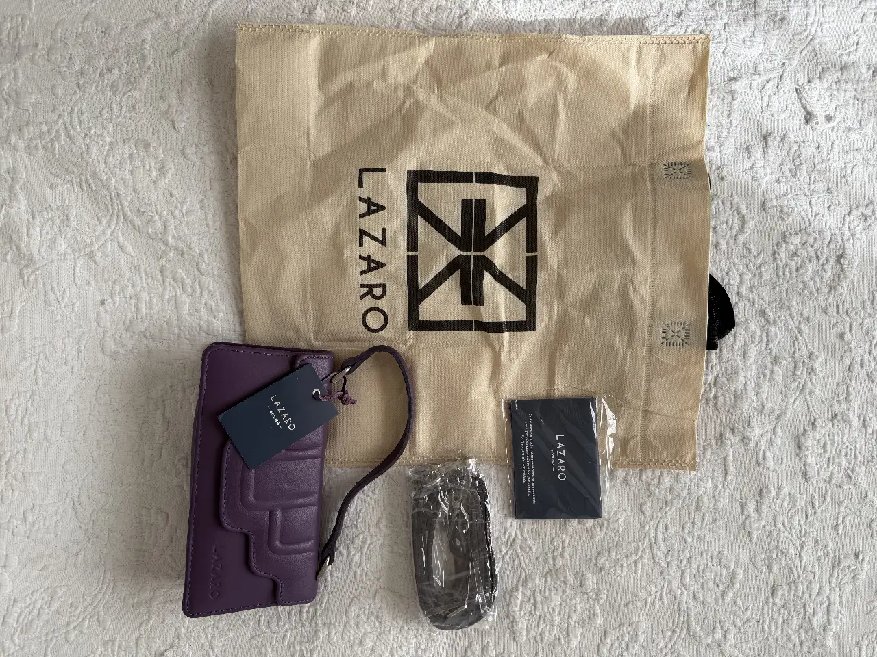 Cartera Lazaro de cuero color violeta con correa para llevar al hombro y correa larga. Incluye bolsa de tela antipolvo para guardarla y espejo de la marca.