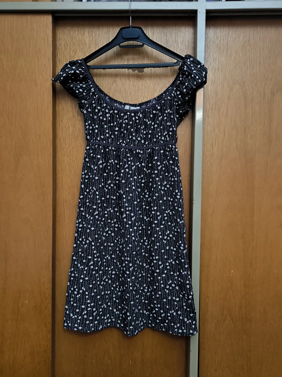 Vestido corto estampado con flores blancas y detalles en morado. Escote Bardot y mangas cortas con volados. Ideal para un look fresco y femenino.