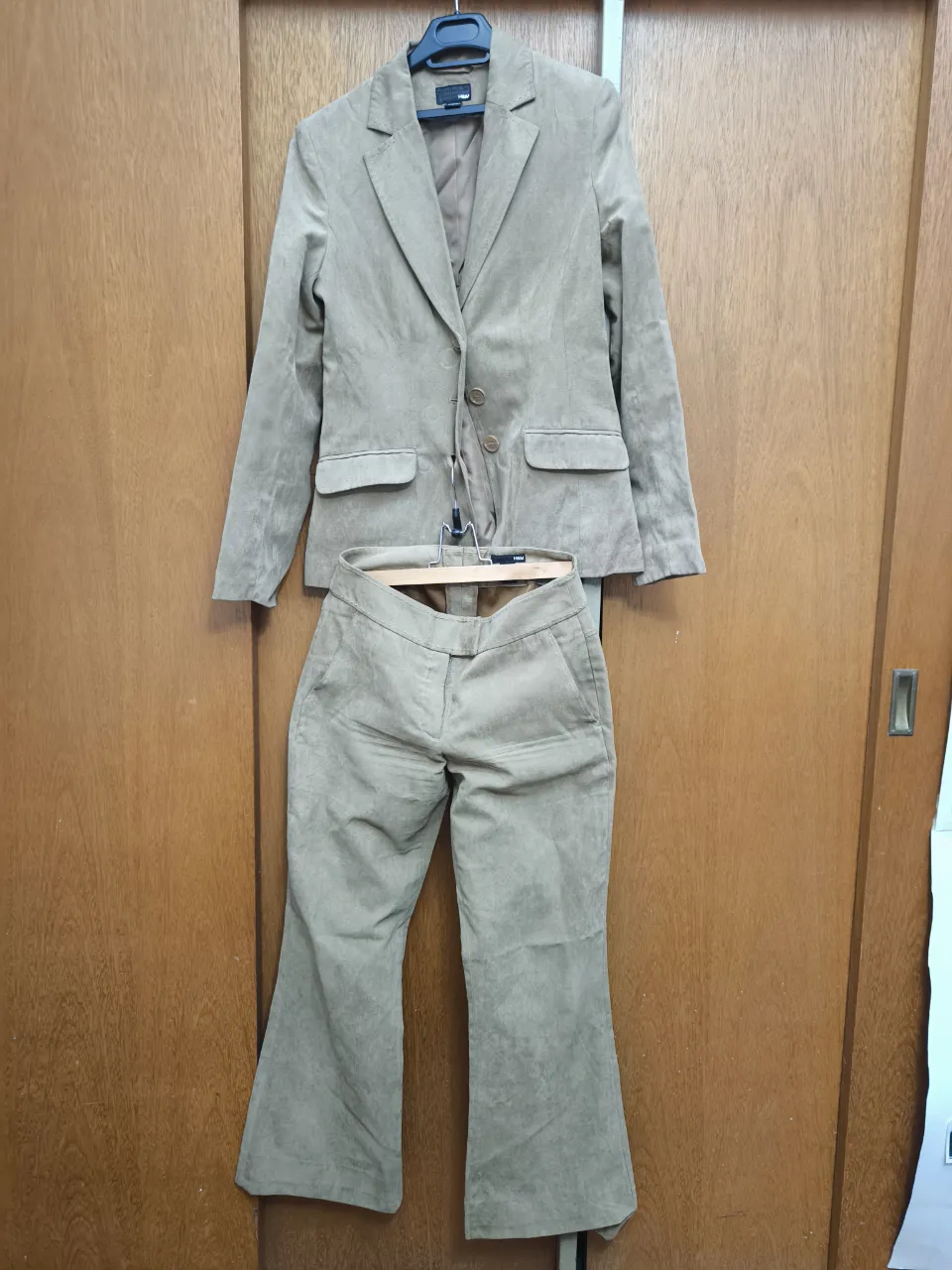 Conjunto sastrero de blazer y pantalón palazzo color beige. El blazer tiene solapa clásica, dos botones al frente y bolsillos con tapa. El pantalón es de tiro alto con pierna ancha y detalles de costura visibles.