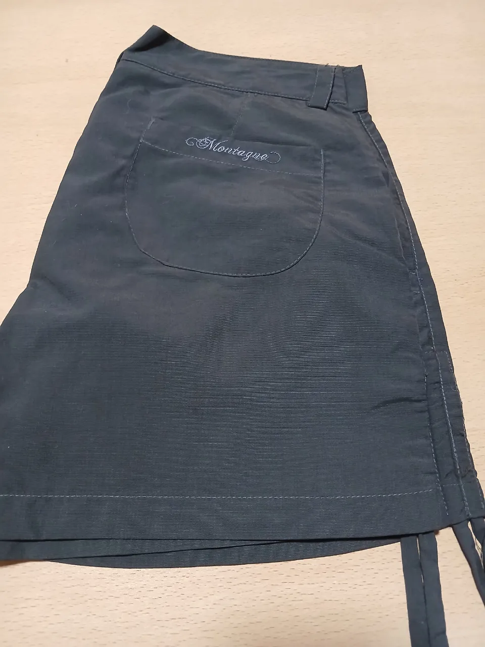 Short deportivo de niña , color gris oscuro, con bolsillo trasero y detalle de la marca Montagne bordada. Ideal para actividades al aire libre.