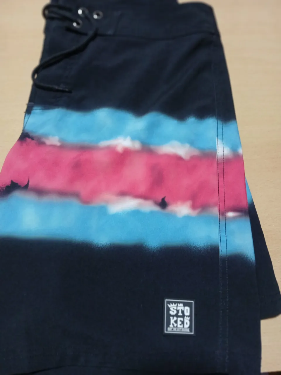 Short de baño Stoked, con diseño a rayas en tonos azul y rosa sobre fondo negro. Ideal para la playa o pileta.