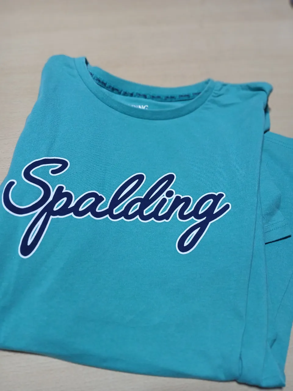 Remera deportiva Spalding de color celeste con estampado blanco. Ideal para entrenar o usar en el día a día.