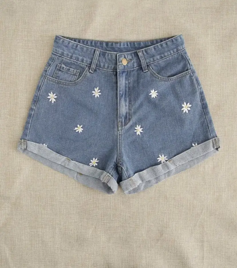 Short de jean azul con bordado de flores blancas. Tiro alto, ideal para el verano. Un clásico renovado con un toque romántico.