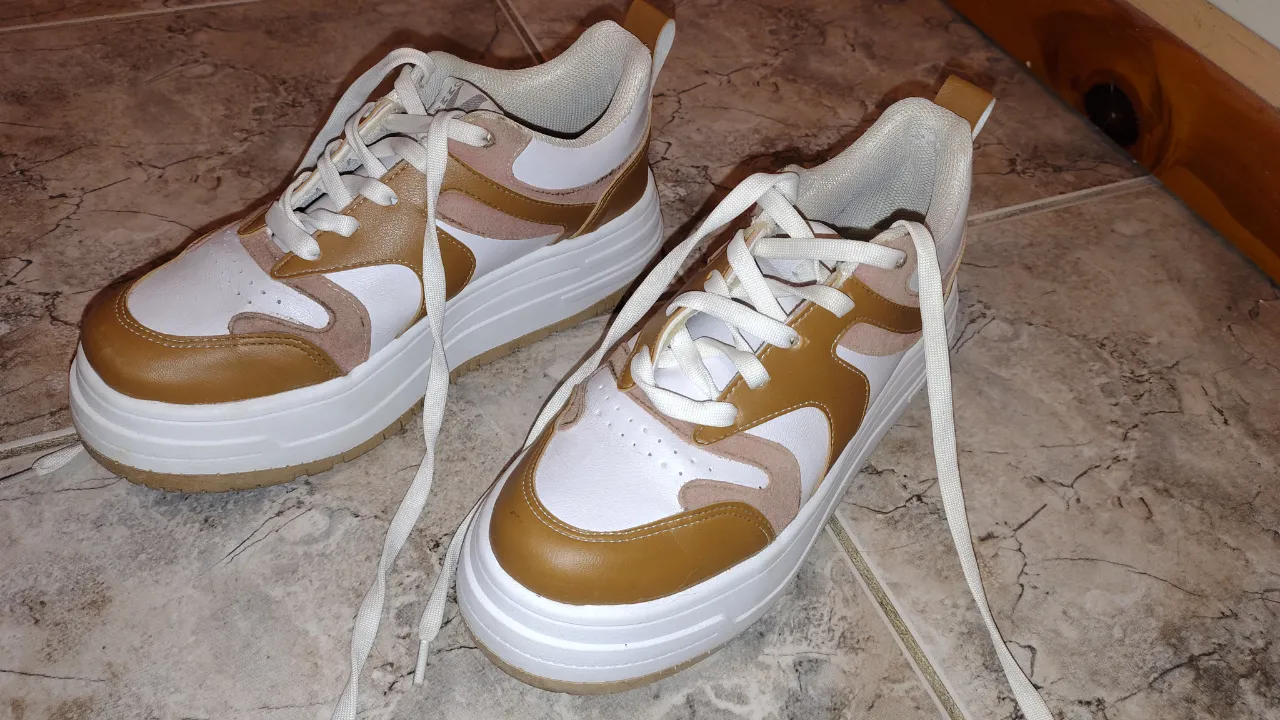 Zapatillas urbanas con plataforma, ideales para el día a día. Combinan blanco, marrón y detalles en rosa pálido, con cordones blancos y suela gruesa. Un toque moderno y canchero para cualquier outfit.