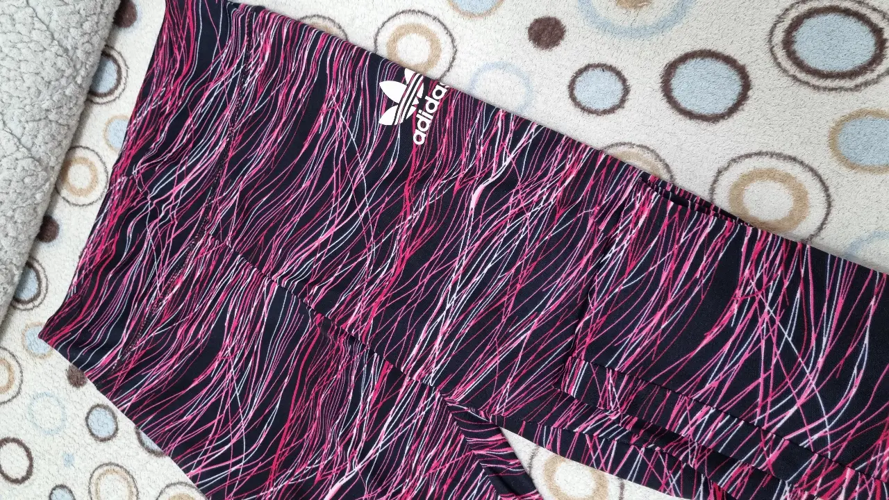 Calzas deportivas Adidas con estampado abstracto en tonos rosa y negro. Ideales para entrenamientos y actividades físicas.