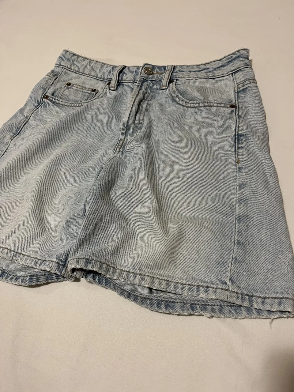 Bermudas de jean tiro medio, color celeste claro, con roturas y detalles deshilachados en el borde inferior. Posee bolsillos delanteros y traseros.