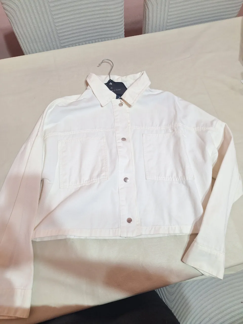Campera de jean blanca, estilo cropped, con bolsillos delanteros y botones. Ideal para un look casual y moderno. Le falta el boton en una manga.