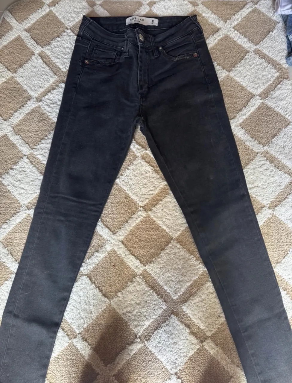 Jeans negros con detalles de desgaste en los bolsillos delanteros. Cierre y botón.