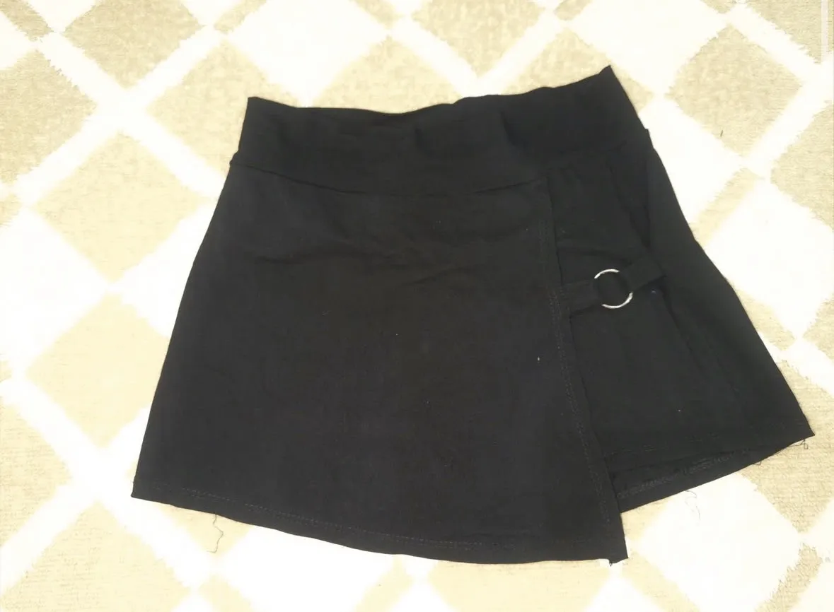 Pollera short negra corta con detalle de argollas metálicas y corte asimétrico.