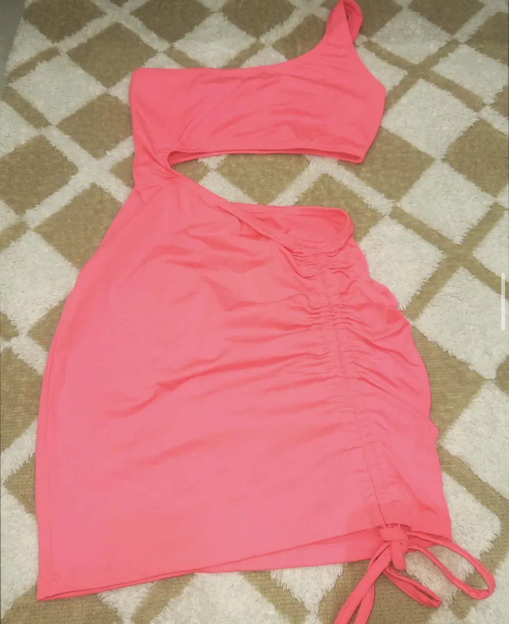 Vestido rosa con un solo hombro y fruncido lateral con cordones ajustables. Posee un recorte en la cintura.