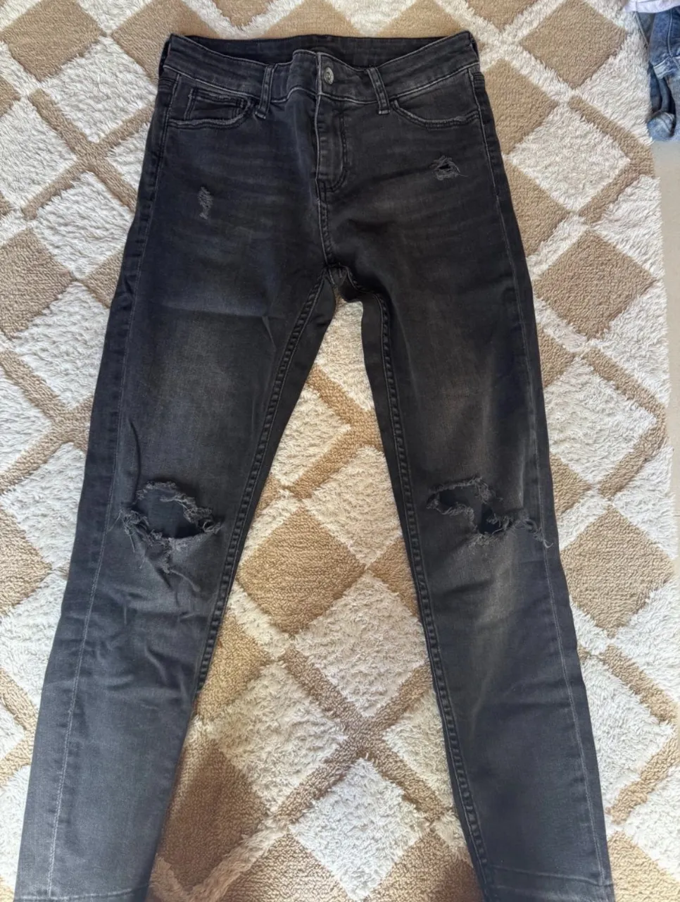 Jean de color gris oscuro con roturas en las rodillas y detalles desgastados.